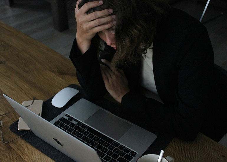Woman with her head in her hands at a laptop during a migraine